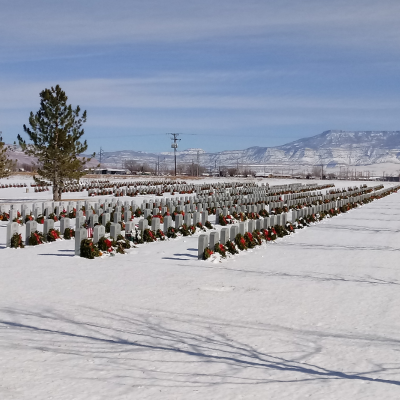 Rows of graves with snow on the ground and wreaths placed on each one.